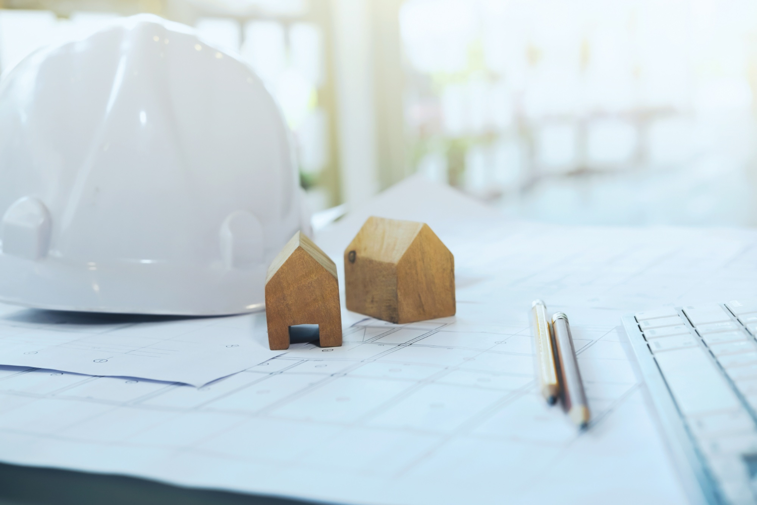 Un casque de chantier est posé sur un plan de maison sur un bureau.