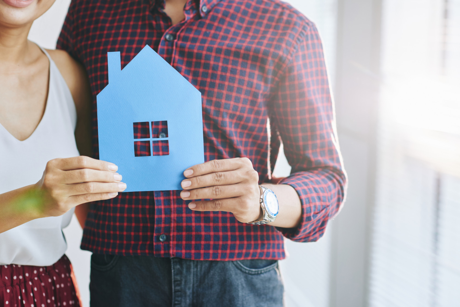 Un couple tient une maison en papier pour illustrer le concept d'acquisition immobilière